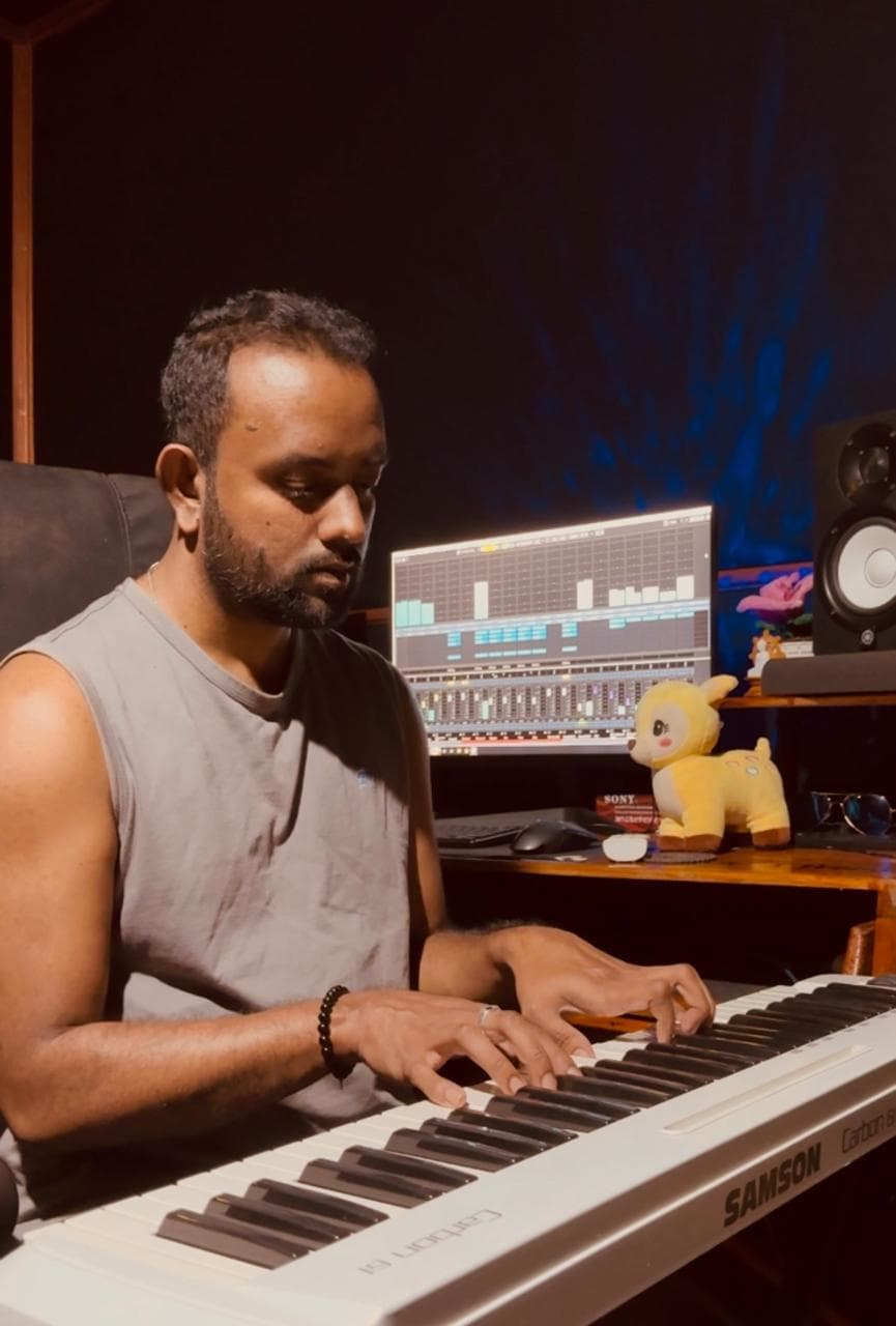 Musician playing a keyboard in front of the main studio production desk and monitor display.